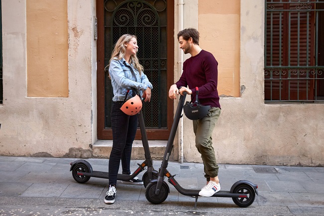 A man and woman are talking while standing on their scooters